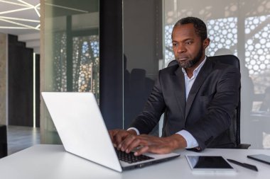 İş yerinde dizüstü bilgisayarda çalışan olgun bir iş adamı, Afro-Amerikan patronu iş elbisesi içinde düşünceli, başarılı bir yatırımcı bankacı..