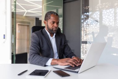 İş yerinde dizüstü bilgisayarda çalışan olgun bir iş adamı, Afro-Amerikan patronu iş elbisesi içinde düşünceli, başarılı bir yatırımcı bankacı..