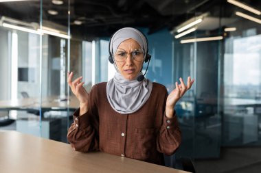 Başörtüsü takmış genç Arap iş kadını portresi ofiste kameranın önünde oturmuş endişe içinde konuşuyor, el ele tutuşuyor, sorunları tartışıyor..