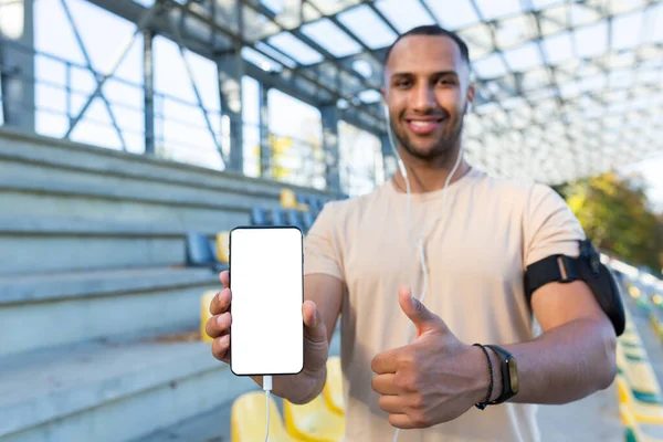 Genç İspanyol sporcu gülümsüyor ve kameraya bakıyor, stadyumda beyaz telefon ekranı gösteren bir adam, koşuyor ve aktif egzersiz yapıyor..