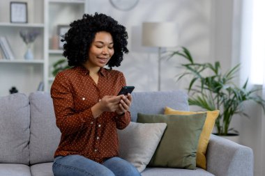 Genç ve güzel bir Afro-Amerikalı kadın evdeki kanepede oturuyor, el ele tutuşan kıvırcık saçlı bir kadın, oturma odasında internetten internet sayfalarını karıştırıyor ve mesajlar yazıyor.