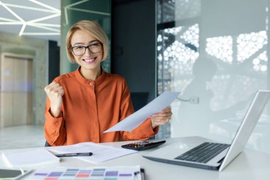 İş yerindeki başarılı ve memnun kadın finansörün portresi, iş kadını gülümseyen, mali rapora bakan iyi başarı elde eden, zaferi kutlayan.