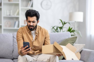 Üzgün ve canı sıkkın bir adam bir paket aldı. Latin Amerikalı teslimat servisinden memnun değildi. Oturma odasındaki kanepede oturdu ve telefonda olumsuz bir eleştiri yazdı..