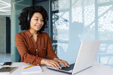 Müşteri hizmetleri çalışanı internetten video görüşmesi için kulaklığı olan ofis içi bilgisayarı olan, klavyede yazan ve uzaktan yardım eden bir kadın..