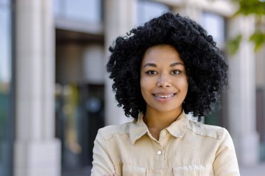 Afrika kökenli Amerikalı bir kadının yakın plan portresi, bir iş kadını gülümseyen ve ofis binasının dışındaki kameraya bakan..