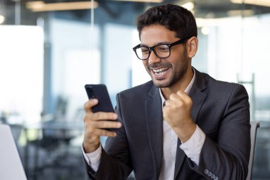 Başarılı iş adamının yakın plan portresi, kazanan telefon, iyi sonuçları kutlayan adam internetten iyi haberler aldı, ofisteki akıllı telefon uygulamasını kullanarak..