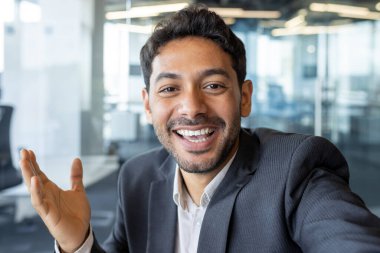 Video dost canlısı konuşma, Arap işadamı iş yerindeki arkadaşlarıyla ve iş arkadaşlarıyla konuşuyor, telefonda uygulama kullanan, gülümseyen ve kameraya el sallayan bir adam..