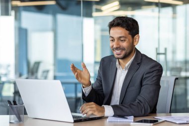 İş yerindeki başarılı Arap iş adamı meslektaşları ve ortaklarıyla uzaktan konuşuyor, video görüşmesi için laptop kullanan adam, tatmin olmuş patron gülümsüyor ve sevinçle el kol hareketi yapıyor..