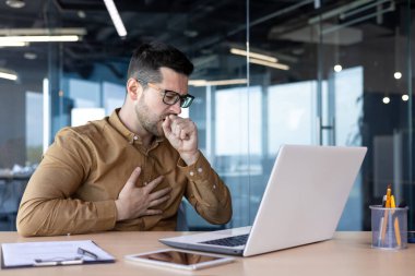 İş yerinde astım krizi. Ofiste laptoplu bir masada çalışan genç bir adam. Öksürüyor, eliyle ağzını kapatıyor, kendini güçsüz hissediyor, virüsten hasta hissediyor..