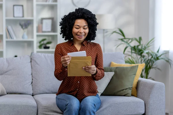 Young African American female student received the results of the exam, interview, admission to the university. He reads the received letter sitting at home on the sofa.