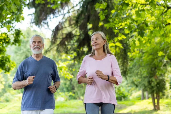 Senior couple of pensioners jogging in the park, gray-haired man and woman joyfully running, active lifestyle.