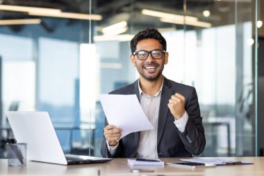 Başarılı Arap finansörünün portresi, deneyimli iş adamı gülümseyen ve kameraya bakan, mali raporu elinde tutan, başarı sonuçlarından memnun olan adam, zafer kazanan jest.