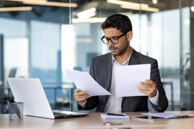 Ciddi bir şekilde konsantre olmuş işadamı evrak işleri arkasında finansör el ele tutuşan raporları okuyor ve kontrol ediyor işyerindeki teknik çözümleri düşünüyor..