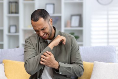 Evdeki kanepede oturan ve elini ve bileğini tutan genç bir Afrikalı Amerikalı 'nın yakın plan fotoğrafı. Kramp, yaralanma, burkulma, kırık..