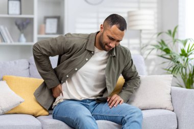 Evdeki kanepede oturan ve arkasını kollayan üzgün Afro-Amerikalı genç adam. Şiddetli ağrı, burkulma, çimdikleme, yaralanma.