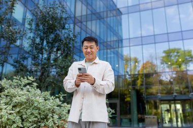 Başarılı bir Asyalı adam günlük kıyafetlerini giyer, telefonu kullanır, şehre modern bir binanın yakınında yürür, mesaj atar, telefon eder, iş çıkışı iş adamı çağırır..