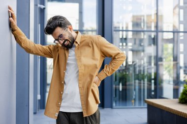 Adamın sırt ağrısı var, aşırı yorgun ve çalışmaktan yorulmuş. Sırtına eliyle masaj yapıyor..