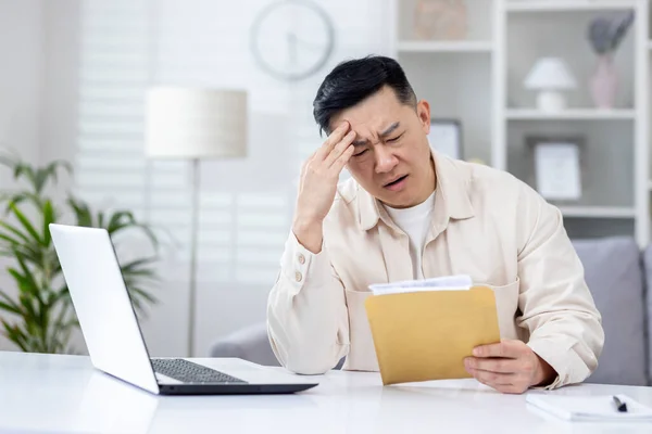 Upset and disappointed man in home office received message mail envelope with bad news, asian man working in home office at desk with laptop.