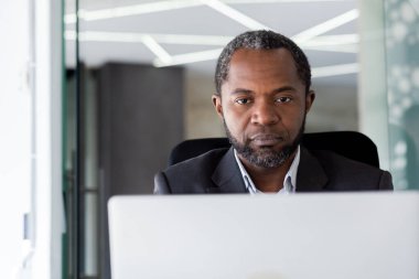 Ciddi düşünen patron iş adamı, yakın plan, dizüstü bilgisayarla çalışan Afro-Amerikan adam, bilgisayar ekranından okuyan ve düşünen adam, ofis içi iş yerinde,.
