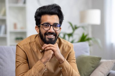 Oturma odasındaki kanepede oturmuş gülümseyen, gülümseyen ve kameraya bakan İspanyol bir adamın yakın plan portresi..