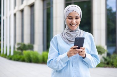 Şehre tesettürlü genç ve güzel bir iş kadını giriyor, Müslüman bir kadın elinde bir telefon tutuyor, akıllı telefondan başvuru yapıyor, gülümsüyor, internette geziniyor..