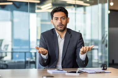 Webcam görüntüsü, çevrimiçi video görüşmesi, web kamerasına ciddi bakan bir adam iş yerindeki iş arkadaşları ve ortaklarıyla konuşuyor..