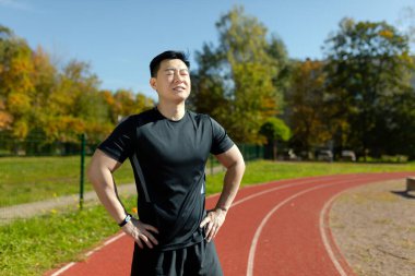 Koşu bandında bir stadyumda ellerini vücudunun kenarlarında tutan gözlerini kapatıp dinlenen Asyalı genç bir adamın portresi..