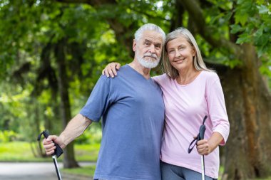 Parkta durmuş birbirine sarılan ve yürüyüş direkleri tutan gri saçlı yaşlı bir adam ve kadının portresi. Birlikte Norveç yürüyüşüne çıkıyorlar..