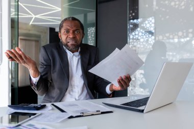 Elinde belgeler, belgeler, anlaşmalar tutan endişeli bir Afro-Amerikalı adamın portresi. Ofiste oturuyor ve hayal kırıklığı içinde kollarını kameraya atıyor..