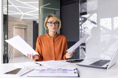 Hayal kırıklığına uğramış iş kadını portresi, kameraya bakan finansör, elinde kötü mali raporlar ve sözleşmeler tutan ofis içinde çalışan kadın muhasebeci..