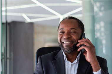 Yetişkin deneyimli, başarılı bir patron telefonda konuşuyor. Yakın plan, Afro-Amerikan bir adam pencereye bakıyor. İş yerinde iş yerinde bilgisayarında iş elbisesi içinde çalışıyor..