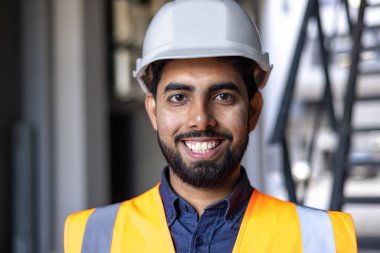 Şapkalı ve yelekli genç mühendisin yakın plan portresi, gülümseyen ve kameraya bakan adam, fabrika işçisi ve lojistik deposunda çalışan adam..