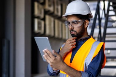 Ciddi düşünme ve fabrikada çelik yelek ve şapka ile çalışan odaklanmış mühendis tablet bilgisayar diyagramı kullanan ve endüstriyel fabrikanın içindeki ekipmanları kontrol eden adam..