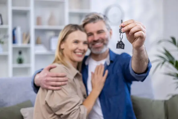 Selected focus, senior gray-haired couple, man and woman hugging together in new apartment house, happy family holding house keys.