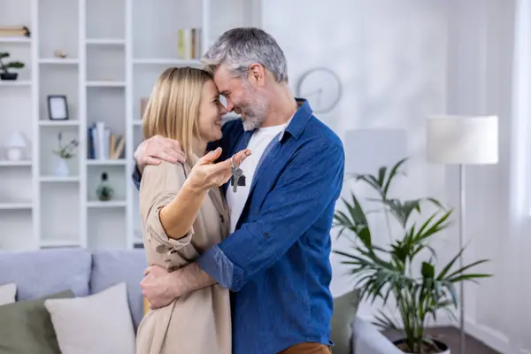 Selected focus, senior gray-haired couple, man and woman hugging together in new apartment house, happy family holding house keys.