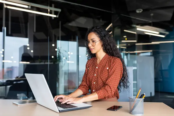 stock image Happy and smiling hispanic businesswoman typing on laptop, office worker with curly hair and glasses happy with achievement results, at work inside office building