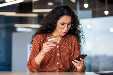 Üzgün ve hayal kırıklığına uğramış bir kadın online fon aktarım hatası, iş yerindeki iş kadını banka kartı ve telefon tutuyor, online dolandırıcılar tarafından aldatılmış..