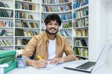 İnternet üzerinden çalışan genç bir Hintli öğrencinin portresi, kütüphanede oturmuş kulaklık takıyor, bir özet yazıyor ve kameraya gülümsüyor..