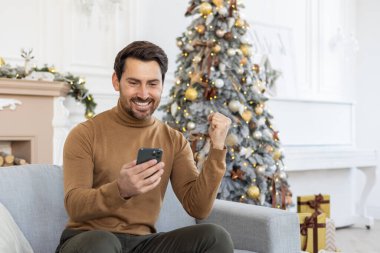 Mutlu bir genç adam haberlere, zafere, telefonda aldığı mesaja sevinir. Evdeki kanepede oturup eliyle evet işareti yapıyor..