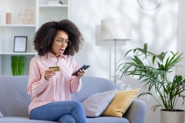 Evdeki kanepede oturan aldatılmış ve hayal kırıklığına uğramış bir kadın, online dolandırıcı. Elinde bir banka kartı ve telefon var. Para transferinin reddedilmesinde bir hata oluştu..