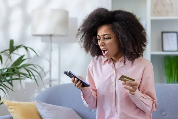 stock image Cheated and disappointed woman sitting on sofa at home, online scammer. He is holding a bank credit card and a phone, he received an error in the refusal of the transfer of funds.