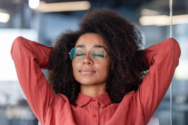 Young beautiful woman resting in the office, business woman with hands behind her head, dozing and dreaming visualizes, thinking about financial achievements of the result, serious with closed eyes.