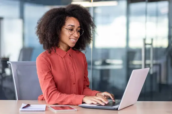 Kırmızı tişörtlü başarılı genç bir kadın bilgisayarla çalışıyor, iş kadını başarıyla gülümsüyor, bilgisayar kullanıyor, klavyede daktilo kullanıyor..