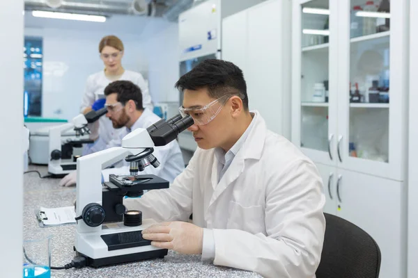 Serious thinking asian scientist working with microscope inside laboratory, man in white medical coat scientist working on sample research.