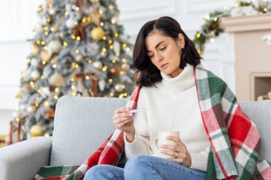 Genç bir kadın yeni yıl tatilinde hastalandı. Dokuz yaşındaki yumurtanın yanındaki kanepede oturuyor, battaniyeyle örtülmüş ve termometreye endişeli bir şekilde bakıyor..