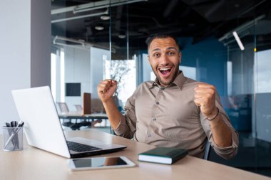 Başarılı Hintli programcı yeni yazılımın başarıyla tamamlanışını kutluyor, kameraya bakan adam, başarı sonuçlarından memnun, dizüstü bilgisayarla çalışıyor, ofis içi, çevrimiçi kazanan.