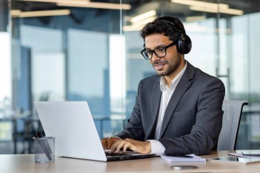 Ofiste bilgisayarla çalışan başarılı Hintli programcı, kulaklıklı ve takım elbiseli adam, klavyede kod yazma, yeni yazılım geliştirme.