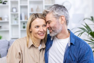 Romantik mutlu orta yaşlı çift evdeki kanepede dinleniyor, gülümsüyor, olgun çifti seviyor rahat oturma odasında dinleniyor, kanepede sarılıyor, birlikte hafta sonunun keyfini çıkarıyor,.