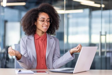 Genç, güzel, başarılı iş kadını Lotus pozisyonunda meditasyon yapıyor ofisin içindeki masada oturuyor, bayan işçi gülümsüyor ve dizüstü bilgisayara bakıyor, mutlu haberler okuyor..