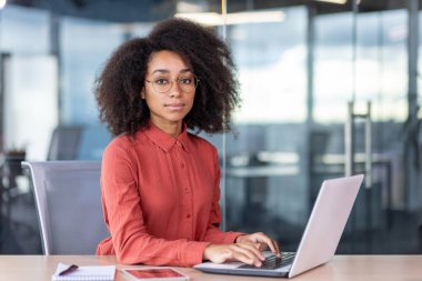 Ofiste bilgisayarla çalışan ciddi odaklı bir kadın, kameraya bakan bir iş kadını, düşünceli ve başarılı bir işçi..
